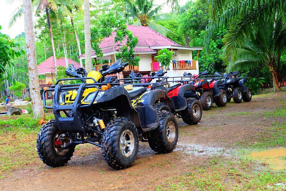 Row of ATVs lined up on a jungle trail beside traditional Thai bungalows for a group activity