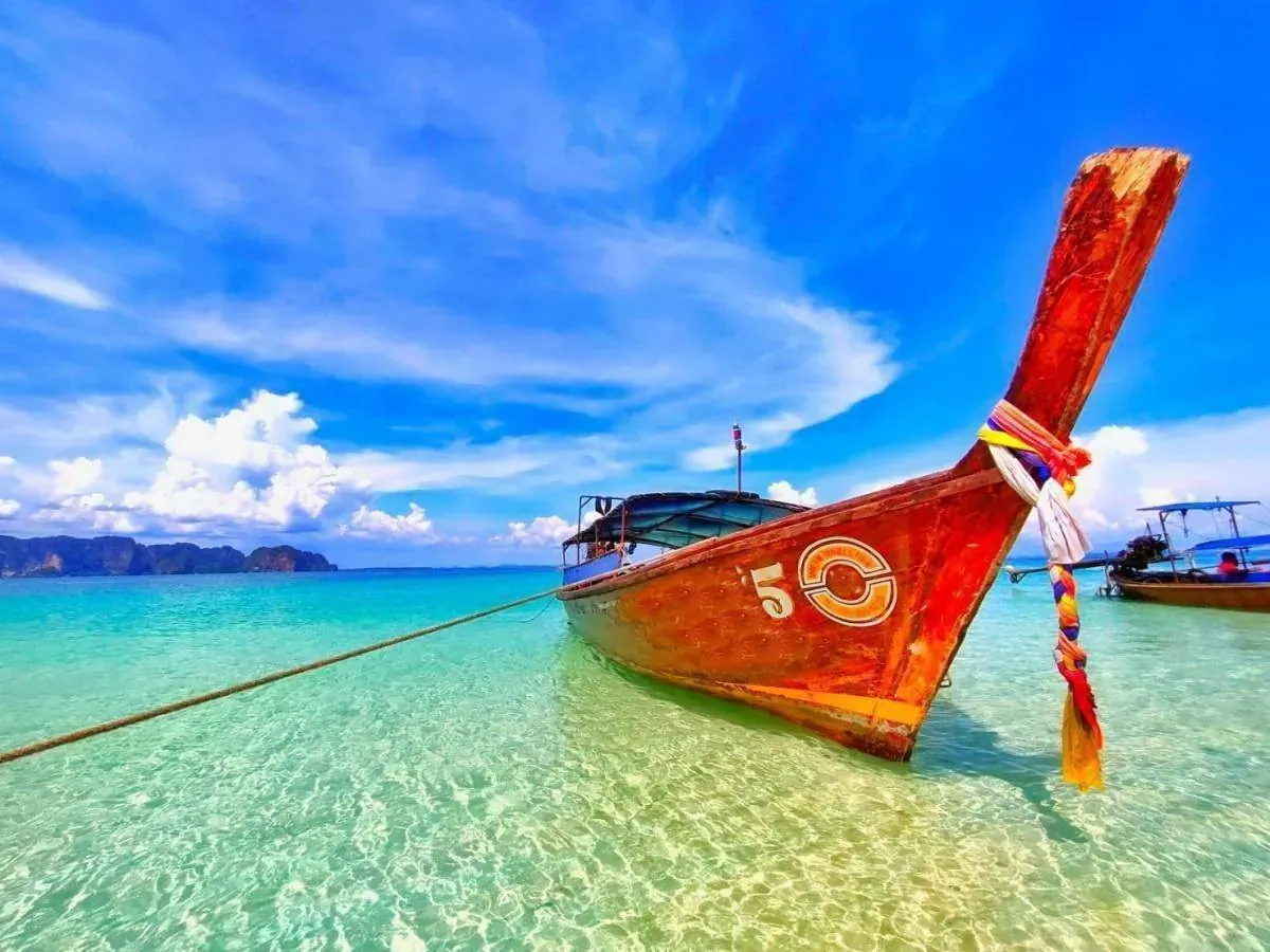 Red longtail boat resting in crystal-clear turquoise water among the limestone islands of Phang Nga Bay