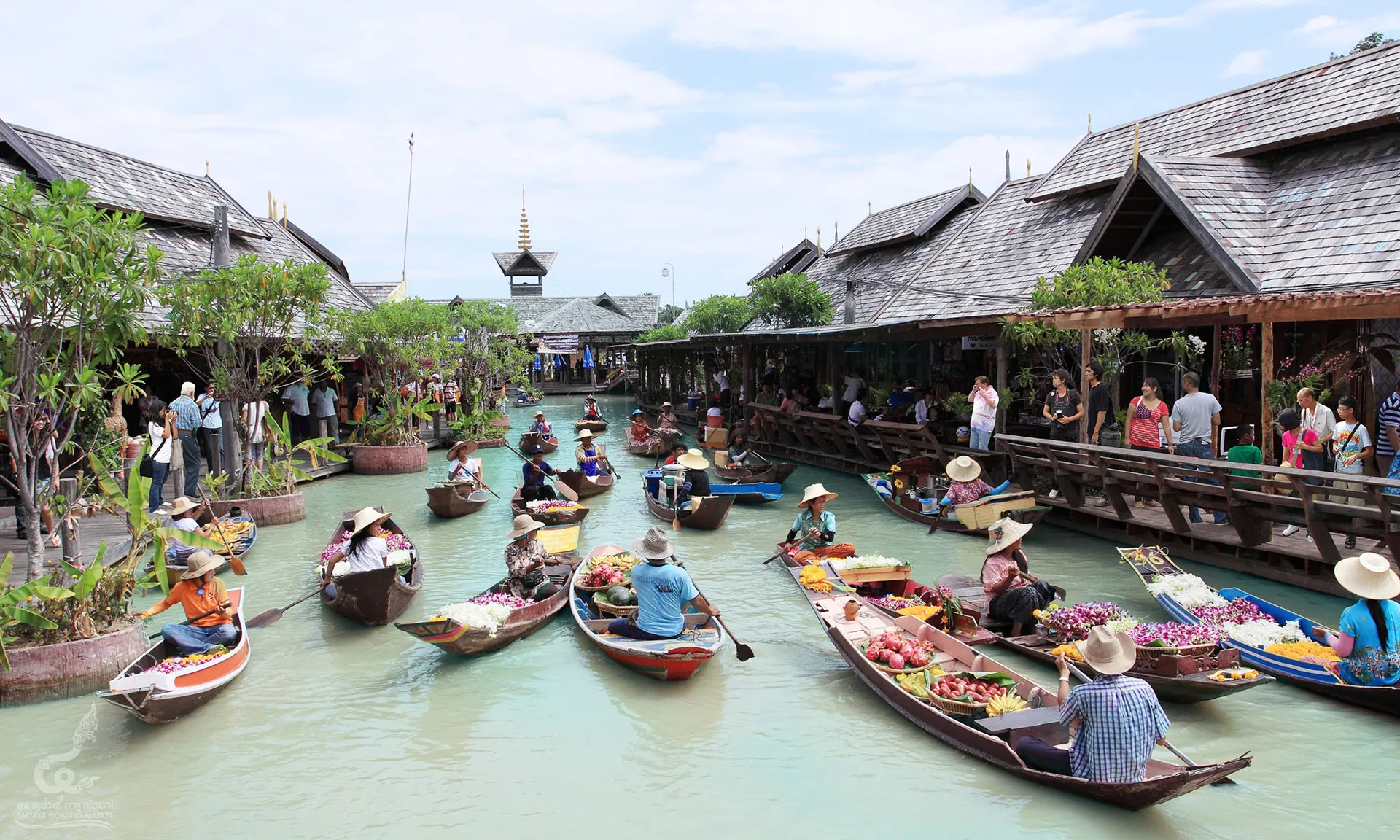 Vendors in straw hats paddling boats loaded with flowers and fruit along the canal at Pattaya Floating Market
