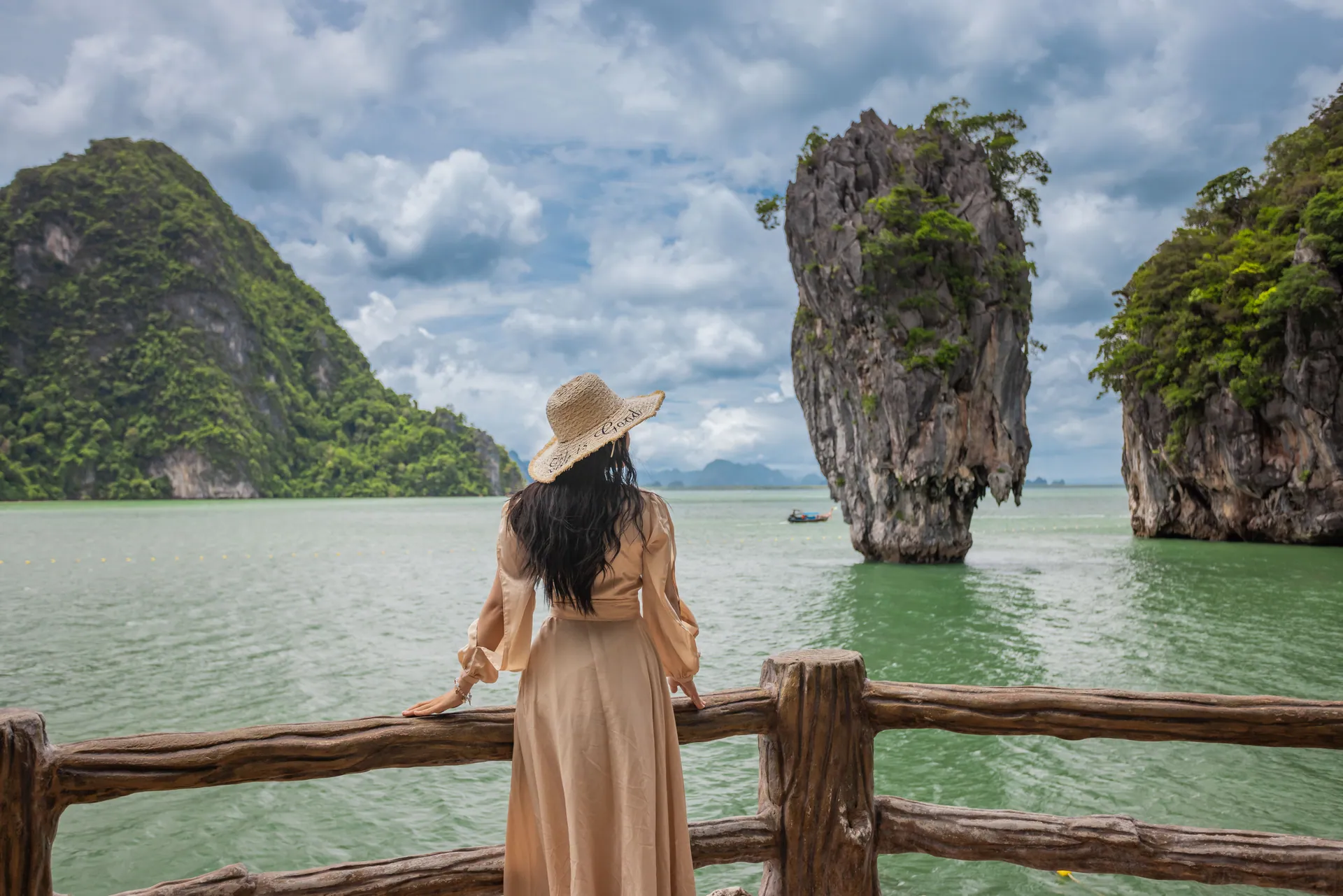 A visitor at a wooden viewpoint railing looking across Phang Nga Bay to James Bond Island