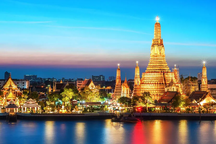 Wat Arun's golden spire glowing above the Chao Phraya River at dusk in Bangkok