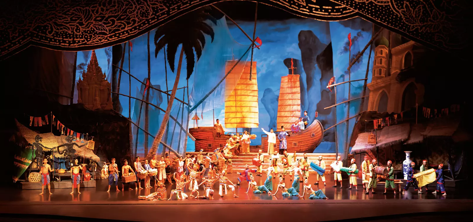 The full cast on stage in traditional costume before a painted junk-ship backdrop at Siam Niramit Phuket